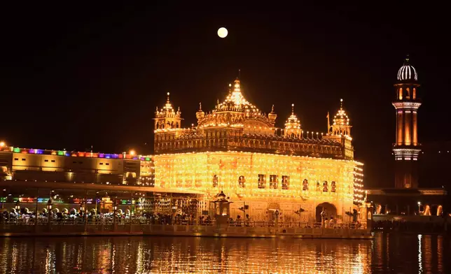 The supermoon rises behind the illuminated Golden Temple as Sikh devotees pray at the to mark the birth anniversary of their first guru, Guru Nanak, in Amritsar, India, Wednesday, Nov. 5, 2025. (AP Photo/Prabhjot Gill)