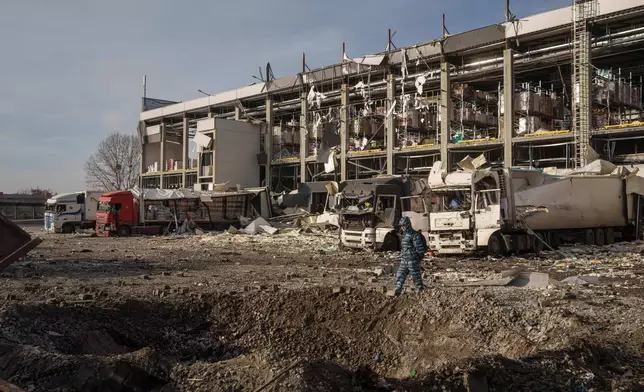 A security guard looks at a crater in front of a Novus logistics center damaged after a Russian strike on Kyiv, Ukraine, on Tuesday, Nov. 25, 2025. (AP Photo/Evgeniy Maloletka)