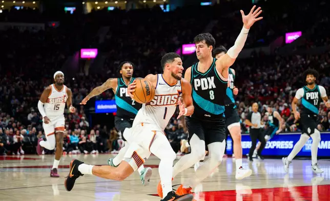 Phoenix Suns guard Devin Booker (1) drives towards the basket past Portland Trail Blazers forward Deni Avdija (8) during the first half of an NBA basketball game on Tuesday, Nov. 18, 2025, in Portland, Ore. (AP Photo/Molly J. Smith)