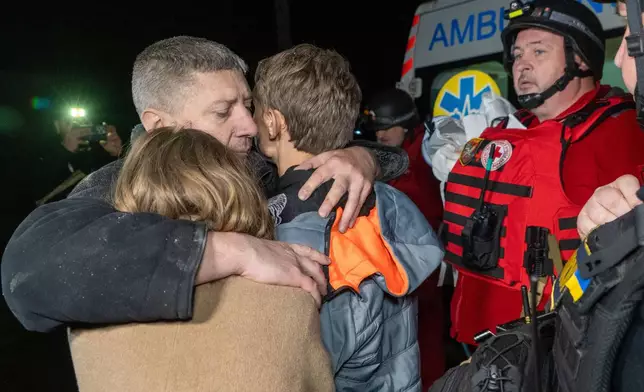 A man hugs his children as they react to the death of their mother killed by a Russian airstrike in Kharkiv, Ukraine, late Sunday, Nov. 23, 2025. (AP Photo/Andrii Marienko)