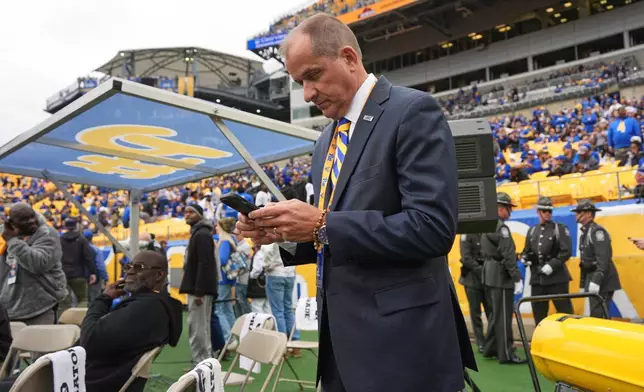 ACC Commissioner Jim Phillips checks his phone on the field before an NCAA college football game between Pittsburgh and Notre Dame in Pittsburgh, Nov. 15, 2025. (AP Photo/Gene J. Puskar)