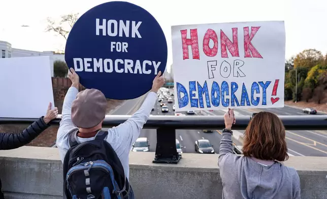 Protesters hold signs amid the arrival of federal law enforcement, Tuesday, Nov. 18, 2025, in Charlotte, N.C. (AP Photo/Matt Kelley)