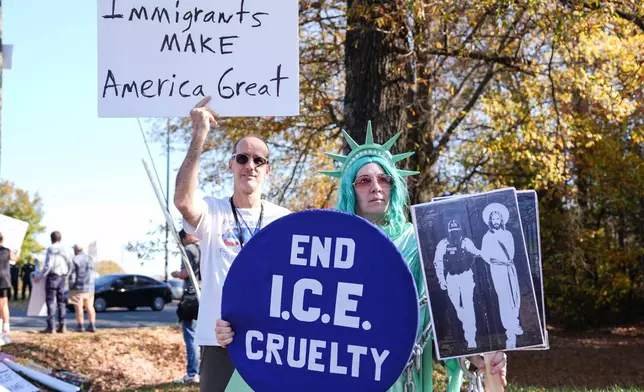 Protesters hold signs during the arrival of federal law enforcement, Wednesday, Nov. 19, 2025, in Charlotte, N.C. (AP Photo/Matt Kelley)