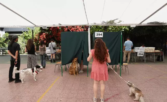 Voters and their dogs line up at a polling station during general elections in Santiago, Chile, Sunday, Nov. 16, 2025. (AP Photo/Cristobal Escobar)