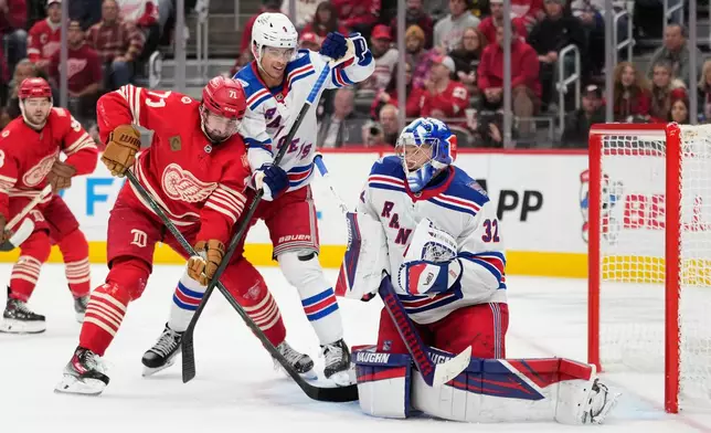 New York Rangers goaltender Jonathan Quick, right, blocks a shot as defenseman Braden Schneider, center, defends Detroit Red Wings center Dylan Larkin during the second period of an NHL hockey game Friday, Nov. 7, 2025, in Detroit. (AP Photo/Ryan Sun)