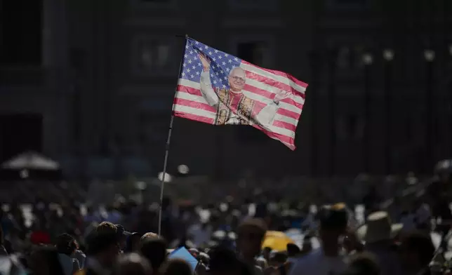 FILE - People wave a flag prior to the arrival of Pope Leo XIV for his weekly general audience in St. Peter's Square at the Vatican, June 18, 2025. (AP Photo/Alessandra Tarantino, File)