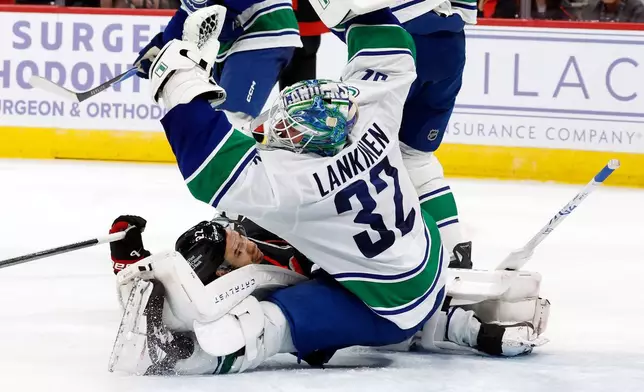 Vancouver Canucks' Kevin Lankinen (32) snares the puck in front of a crashing Carolina Hurricanes' Logan Stankoven (22) during the second period of an NHL hockey game in Raleigh, N.C., Friday, Nov. 14, 2025. (AP Photo/Karl DeBlaker)