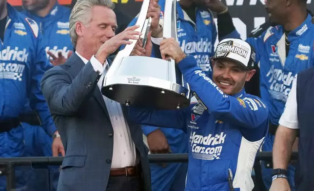 Kyle Larson receives the trophy from NASCAR Commissioner Steve Phelps after winning the NASCAR Cup Series championship Sunday, Nov. 2, 2025, in Avondale, Ariz. (AP Photo/Rick Scuteri)