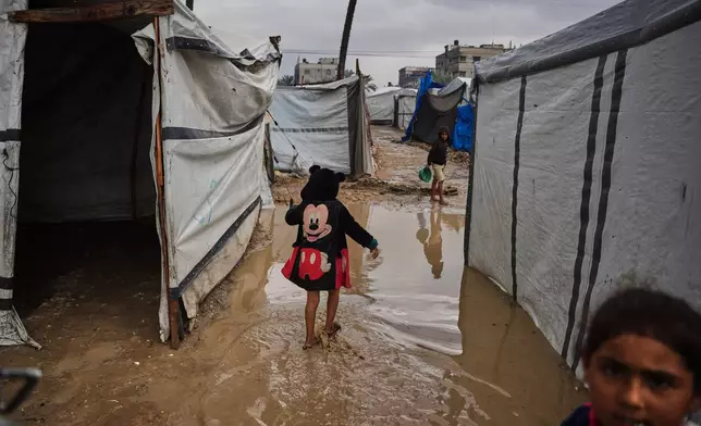 Palestinians walk through a flooded temporary tent camp after heavy rainfall in Deir al-Balah, central Gaza Strip, Tuesday, Nov. 25, 2025. (AP Photo/Abdel Kareem Hana)