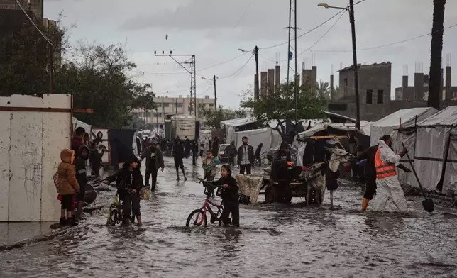 Palestinians walk through a flooded street next to a temporary tent camp after heavy rainfall in Deir al-Balah, central Gaza Strip, Tuesday, Nov. 25, 2025. (AP Photo/Abdel Kareem Hana)