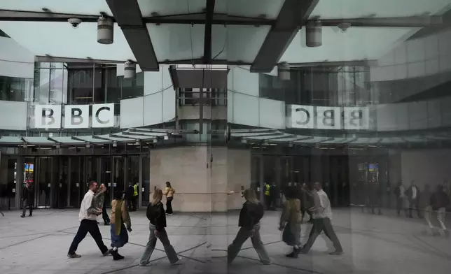 Pedestrians are reflected as they walk outside BBC Broadcasting House in London, Tuesday, Nov. 11, 2025. (AP Photo/Kirsty Wigglesworth)