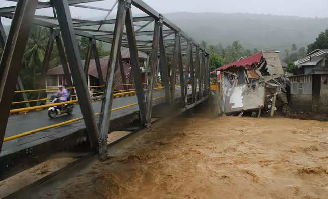 Motorists ride on a bridge past buildings damaged by flooding in Tanah Datar, West Sumatra, Indonesia, Friday, Nov. 28, 2025. (AP Photo/Ali Nayaka)