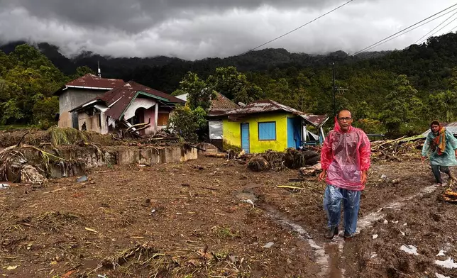 People walk past damaged houses at a village affected by flood in Malalak, West Sumatra, Indonesia, Friday, Nov. 28, 2025. (AP Photo/Ade Yuandha)