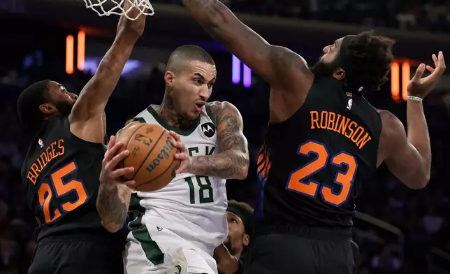 Milwaukee Bucks forward Kyle Kuzma (18) drives between New York Knicks center Mitchell Robinson (23) and Mikal Bridges (25) during the first half of an NBA basketball game, Friday, Nov. 28, 2025, in New York. (AP Photo/Adam Hunger)