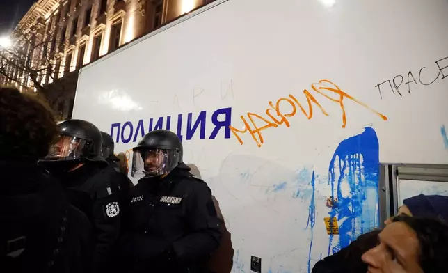 Policeman stand near a vandalized police vehicle with a graffiti sign "mafia," as thousands took to the streets of Bulgaria's capital, Sofia, to denounce steep tax hikes in next year's draft budget before being finally voted on in parliament, Wednesday, Nov 26, 2025. (AP Photo/Valentina Petrova)