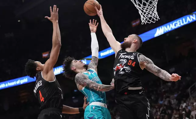 Toronto Raptors forward/center Sandro Mamukelashvili (54) rejects a shot by Charlotte Hornets guard Lamelo Ball, center, as Raptors forward/guard Scottie Barnes (4) looks on during first-half NBA basketball game action in Toronto, Monday, Nov. 17, 2025. (Nathan Denette/The Canadian Press via AP)