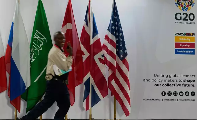 A journalist walks flags of participating country's at the media centre of the G20 Summit in Johannesburg, South Africa, Friday, Nov. 21, 2025. (AP Photo/Themba Hadebe)