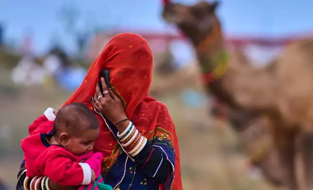 A woman holds her child as she talks on a phone at the annual cattle fair in Pushkar, in the western Indian state of Rajasthan, Sunday, Oct. 26, 2025. (AP Photo/Rajesh Kumar Singh)