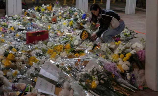 A woman lays flowers near the site of the deadly Wednesday fire at Wang Fuk Court, a residential estate in the Tai Po district of Hong Kong's New Territories on Saturday, Nov. 29, 2025. (AP Photo/Ng Han Guan)