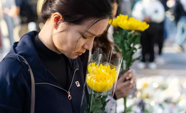 People holds flower near the site to mourn the victims of the deadly Wednesday fire at Wang Fuk Court, a residential estate in the Tai Po district of Hong Kong's New Territories on Saturday, Nov. 29, 2025. (AP Photo/Chan Long Hei)