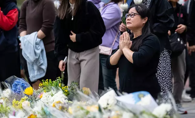 People offer flowers and pray for the victims near the site of a deadly Wednesday fire at Wang Fuk Court, a residential estate in the Tai Po district of Hong Kong's New Territories on Sunday, Nov. 30, 2025. (AP Photo/Chan Long Hei)
