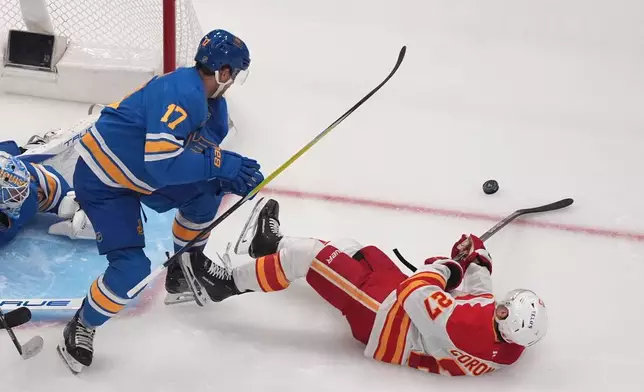 Calgary Flames' Matt Coronato (27) and St. Louis Blues' Cam Fowler (17) battle for a loose puck during the second period of an NHL hockey game Tuesday, Nov. 11, 2025, in St. Louis. (AP Photo/Jeff Roberson)