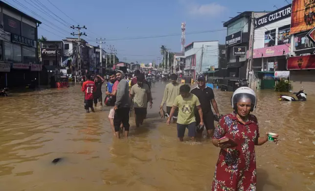 People wade through a submerged area of Colombo, Sri Lanka, following flooding on Sunday, Nov. 30, 2025. (AP Photo/Eranga Jayawardena)
