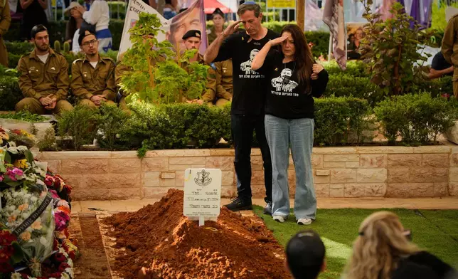 Ruby and Hagit Chen salute over the grave of their son, slain hostage Israeli-American Staff Sgt. Itay Chen during his funeral at Kiryat Shaul Cemetery in Tel Aviv, Israel, Sunday, Nov. 9, 2025, after his body was returned from Gaza. (AP Photo/Ohad Zwigenberg)