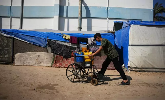 A Palestinian youth pushes a cart loaded with jerrycans filled with water after collecting it at a camp for displaced people in Deir al-Balah, central Gaza Strip, Saturday, Nov. 1, 2025. (AP Photo/Abdel Kareem Hana)