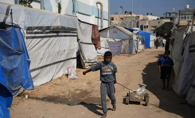 A Palestinian child pulls a cart between tents temporarily erected in a camp in Deir al‑Balah, central Gaza Strip, Saturday, Nov. 1, 2025. (AP Photo/Abdel Kareem Hana)
