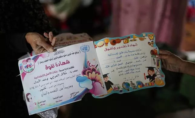 Tahreer al-Awaini, 33, holds her daughter's prewar certificates inside a classroom where she and her children now live, in Khan Younis, Gaza, Wednesday, Nov. 12, 2025. The school was bombarded in July 2024 during the Israel-Hamas war. (AP Photo/Abdel Kareem Hana)