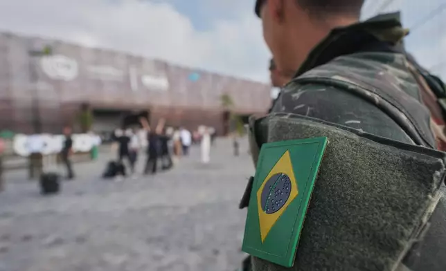 An image of the Brazil flag is visible on security personnel outside the venue for the COP30 U.N. Climate Summit, Tuesday, Nov. 18, 2025, in Belem, Brazil. (AP Photo/Andre Penner)