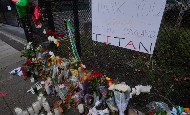 Flowers and signs are displayed at a sidewalk memorial for former Oakland football coach John Beam at Laney College, in Oakland, Calif., Monday, Nov. 17, 2025. (AP Photo/Jeff Chiu)
