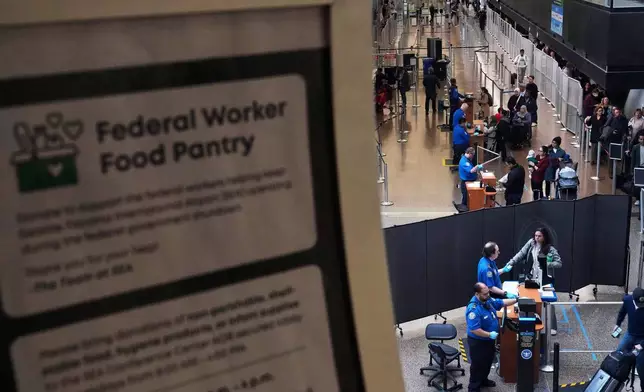 A sign for a food pantry for federal workers is seen as TSA agents check identification at a security checkpoint at Seattle-Tacoma International Airport, Thursday, Nov. 6, 2025, in SeaTac, Wash. (AP Photo/Lindsey Wasson)