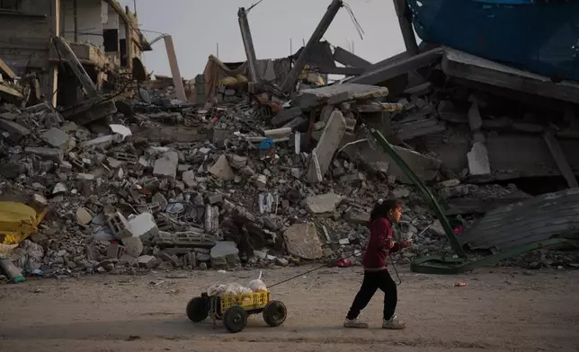 A girl carries bread as she walks past destruction left by Israeli air and ground operations in Gaza City Saturday, Nov. 29, 2025. (AP Photo/Abdel Kareem Hana)