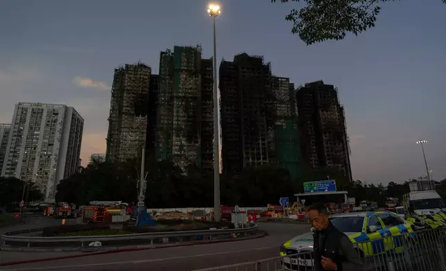 A man walks past charred buildings burnt after a deadly fire that started Wednesday at Wang Fuk Court, a residential estate in the Tai Po district of Hong Kong's New Territories, Friday, Nov. 28, 2025. (AP Photo/Ng Han Guan)