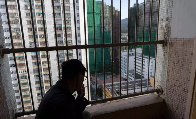A resident smokes as he looks out towards buildings burnt after a deadly fire that started Wednesday at Wang Fuk Court, a residential estate in the Tai Po district of Hong Kong's New Territories, Friday, Nov. 28 2025. (AP Photo/Ng Han Guan)