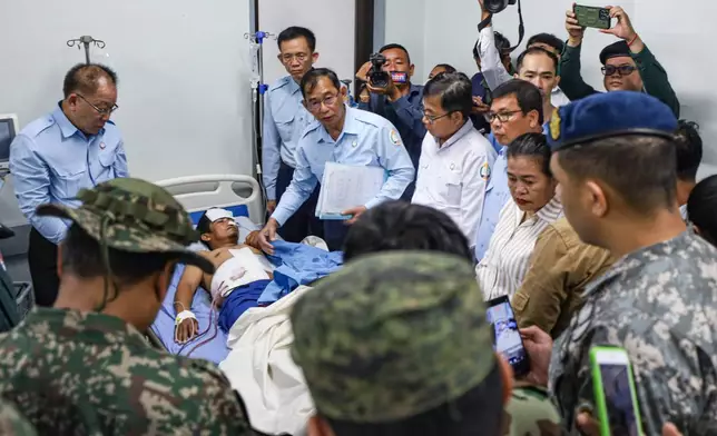 In this photo released by Agence Kampuchea Press (AKP), an injured man, rear center, is visited by members of the ASEAN's observer team (AOT) in a hospital in Prey Chan, a border village to Thailand, in Banteay Meanchey province, Cambodia, Thursday, Nov. 13, 2025. (AKP via AP)
