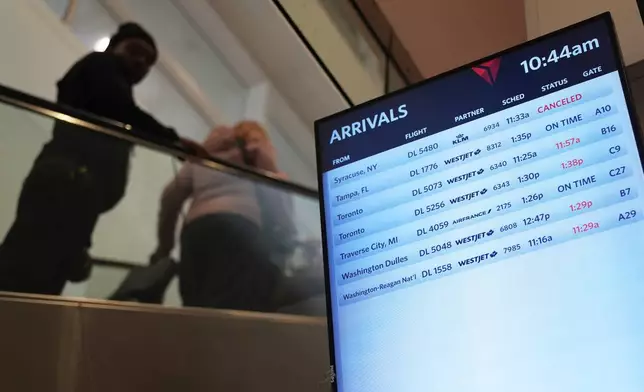 Travelers walk past a video board at the Detroit Metropolitan Airport, Sunday, Nov. 9, 2025, in Detroit. (AP Photo/Ryan Sun)