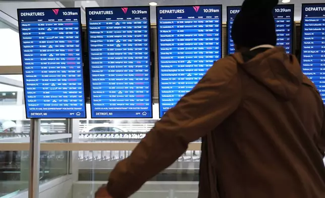 Travelers wait at a video board at the Detroit Metropolitan Airport, Sunday, Nov. 9, 2025, in Detroit. (AP Photo/Ryan Sun)