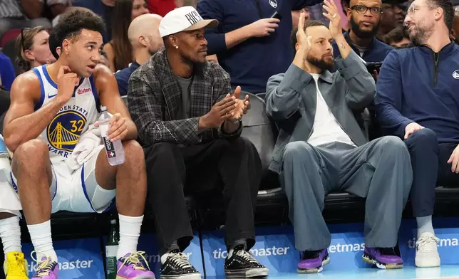 Golden State Warriors forward Jimmy Butler III, second from second, and guard Stephen Curry, second from right, applaud during the first half of an NBA basketball game against the Miami Heat, Wednesday, Nov. 19, 2025, in Miami. (AP Photo/Lynne Sladky)