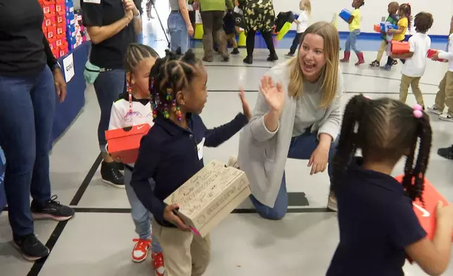 FILE - A volunteer waves to a student as she waits in line at Miles Intermediate Elementary School in Atlanta after receiving new shoes from Mercedes-Benz USA, as a part of their Season to Shine holiday program, on Dec. 7, 2022. (AP Photo/Sharon Johnson, File)