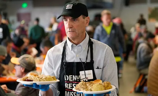 FILE - Volunteer Brent Cohen carries plates of food to guests during the annual Thanksgiving banquet at the Denver Rescue Mission on Nov. 22, 2023, in Denver. (AP Photo/David Zalubowski, File)