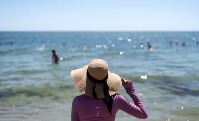 Ruth Wilson, who has lupus and is sensitive to the sun, stands at the water's edge while at the beach with family, Saturday, Aug. 16, 2025, in South Yarmouth, Mass. (AP Photo/David Goldman)