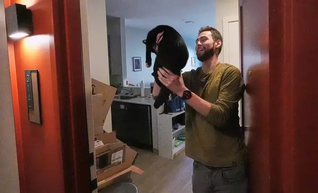 Austin Geary holds up his cat, Jojo, who greeted him at his apartment door, at the Pok Oi Residences, Oct. 17, 2025, in the Chinatown neighborhood of Boston. (AP Photo/Charles Krupa)