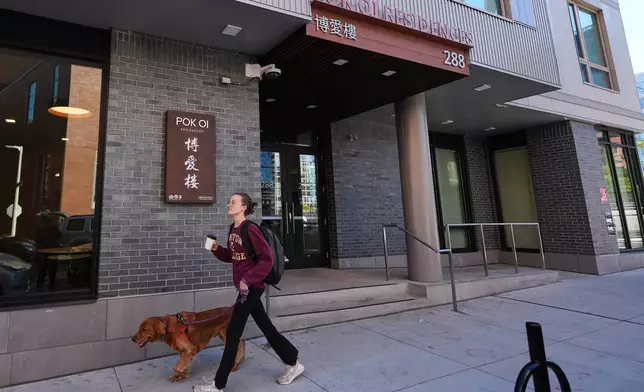 A woman walks her dog past the Pok Oi Residences, Oct. 17, 2025, in the Chinatown neighborhood of Boston. (AP Photo/Charles Krupa)