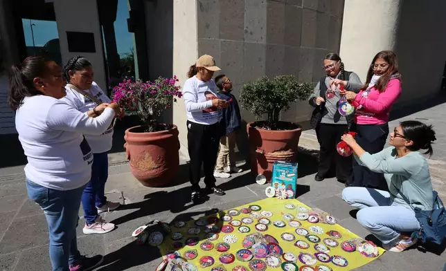 People whose relatives have gone missing decorate Christmas ornaments with photographs of their missing loved ones to hang on the Tree of Hope during an event organized by the diocese of Ecatepec at the Church of the Sacred Heart of San Cristobal in Ecatepec, State of Mexico, Monday, Nov. 17, 2025. (AP Photo/Ginnette Riquelme)