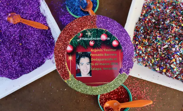 A photograph of Argenis Yosimar Pensado Barrera, who disappeared on March 16, 2014 in Xalapa, Veracruz state, covers a Christmas ornament to hang on the Tree of Hope, during an event organized by the diocese of Ecatepec at the Church of the Sacred Heart of San Cristobal in Ecatepec, State of Mexico, Monday, Nov. 17, 2025. (AP Photo/Ginnette Riquelme)