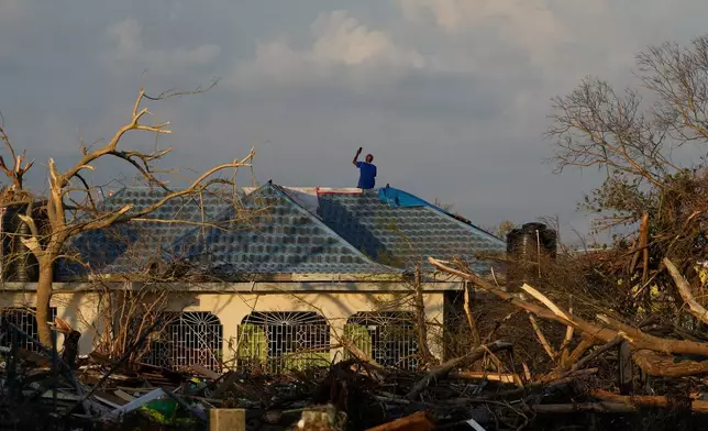 A man searches for cell signal from the roof of his house flooded and damaged by Hurricane Melissa in Black River, Jamaica, Thursday, Oct. 30, 2025. (AP Photo/Matias Delacroix)