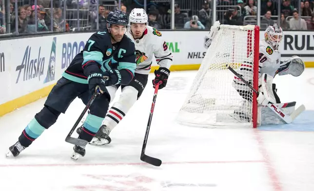Seattle Kraken right wing Jordan Eberle (7) and Chicago Blackhawks defenseman Artyom Levshunov (55) compete for the puck as goalie Arvid Soderblom (40) looks on during the first period of an NHL hockey game Monday, Nov. 3, 2025, in Seattle. (AP Photo/Jason Redmond)